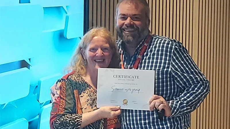 Two service users are attending an awards ceremony, holding an award and smiling for a photo