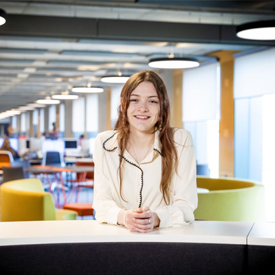 A female with long brown hair wearing a white blouse is in the Catalyst building