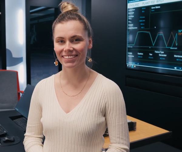 A female apprentice wearing a beige jumper is smiling in a technology office at Capula