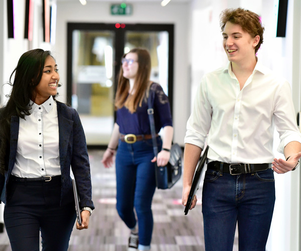 A smartly dressed female and male student are walking and chatting in an office hallway