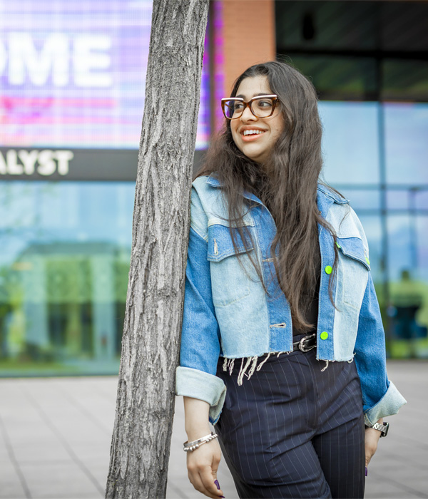 A young female student wearing a denim jacket is smiling standing outside the Catalyst