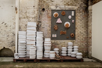 Ceramic installation of stacked white plates and wall-mounted pieces in an industrial gallery.
