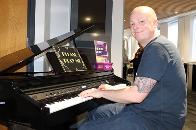 Smiling man sits at a grand piano with sheet music open on the stand.