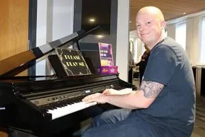 Smiling man sits at a grand piano with sheet music open on the stand.