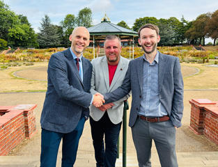 Three men stood outside smiling and shaking hands