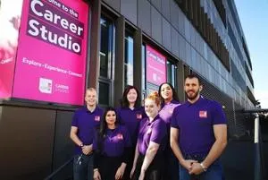 Six career coaches in purple shirts pose outside the magenta Career Studio windows.
