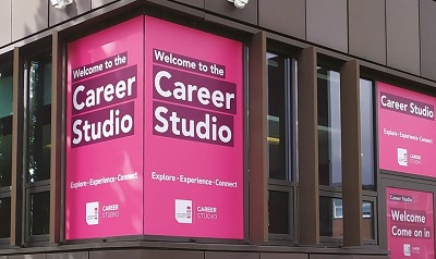 Campus windows wrapped in magenta signs reading 'Welcome to the Career Studio.'