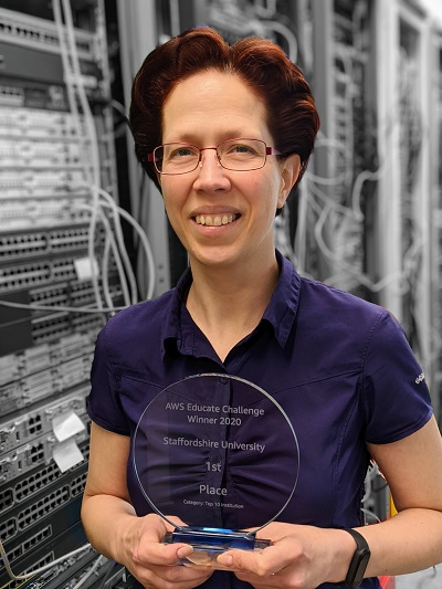 Woman holds a transparent award while standing in front of rows of computer servers.