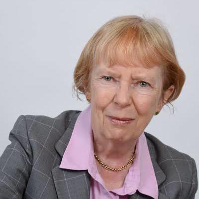 A woman with short light coloured hair wearing a shirt and blazer smiling at the camera