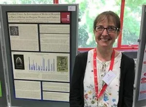 Smiling woman stands beside a detailed academic research poster at a conference.