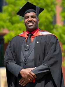 A smiling man wearing a  graduation cap and gown