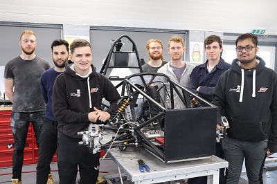 Formula Student team poses around the exposed frame of a single-seat racing car.