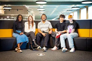 Five smiling students sat together on a sofa