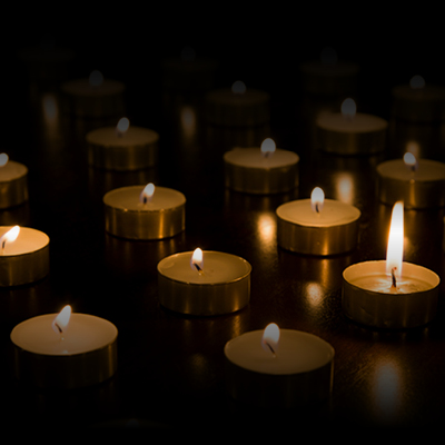 Rows of small memorial candles glow against a black background.