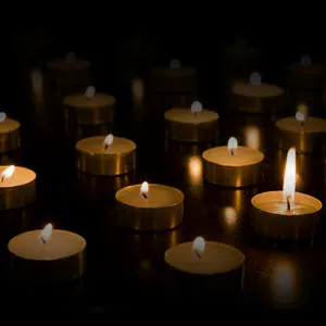 Rows of small memorial candles glow against a black background.