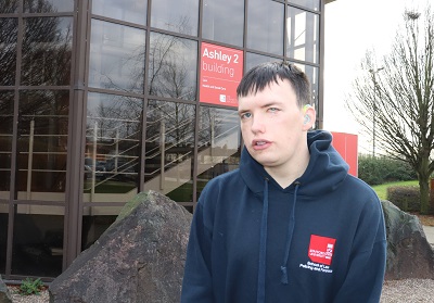 Young man in a dark university hoodie stands outside the Ashley 2 building.