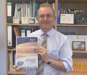 Man in an office holds a report titled 'Environmental Health Inequalities in Europe.'