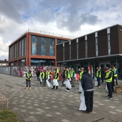 Volunteers in high-visibility vests gather outside a campus building for a litter pick.