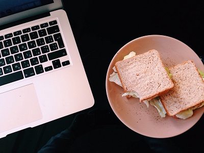 Laptop and a plate of sandwiches sit side by side on a dark desk.