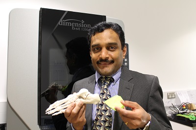 Man in a suit holds a skeletal foot model and a yellow insole beside a display screen.