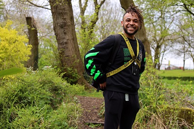 Smiling man in black sportswear and medals stands among trees in a park.