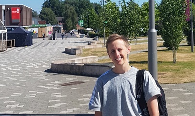 Young man with a backpack stands on a sunny university walkway.