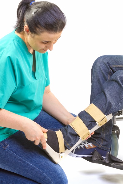 Clinician in green scrubs fits a wooden and fabric orthotic support around a seated person's leg.