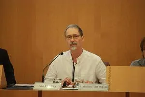 Older man in a white shirt speaks into a microphone at an international conference panel.