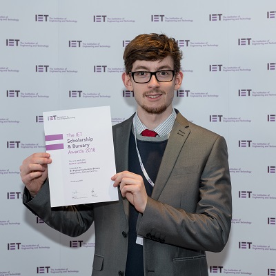 Young man in a suit holds an IET Engineering Horizons Bursary certificate.