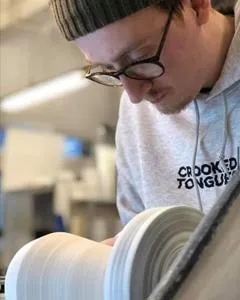 Student concentrates while shaping a ceramic vessel on a pottery wheel.