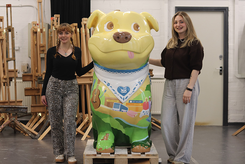 Students Grace Jones and Amy Watkins stood either side of a decorated Staffy Staffordshire Bull Terrier sculpture
