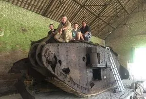 Four people sit and stand on a historic tank displayed inside a brick barn.