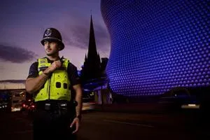 Police officer stands at night in Birmingham with the illuminated Bullring building behind.