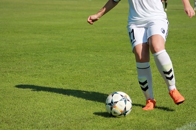 Lower body of a footballer in a white kit dribbling a ball across a green pitch.