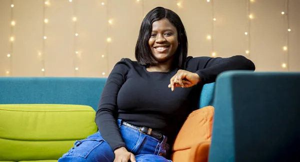 A female with black hair is sitting relaxed smiling in a colourful blue sofa