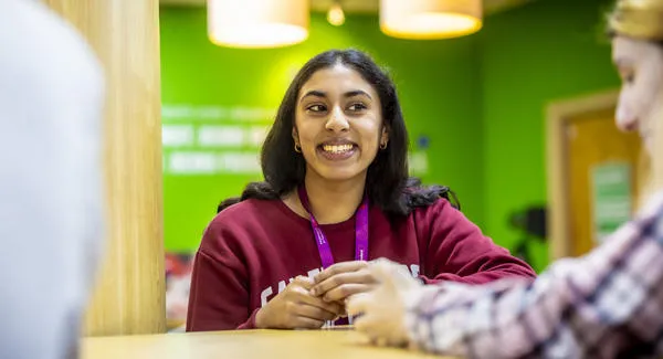 A young female student with long black hair is wearing a red sweatshirt she is smiling