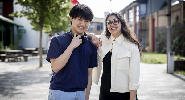 A young male and a female student and standing casually together on Leek Road campus smiling