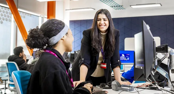 A female lecturer is chatting with a student in the computer lab, they are both smiling