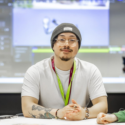 A male wearing a grey beanie hat is sat at a table in a collaborative room