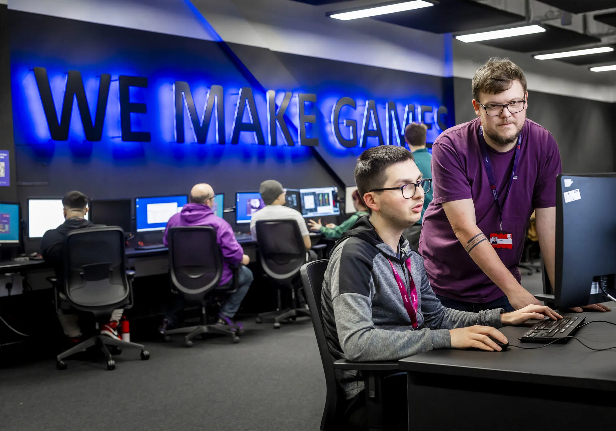 A male academic is helping a male student at his PC desk